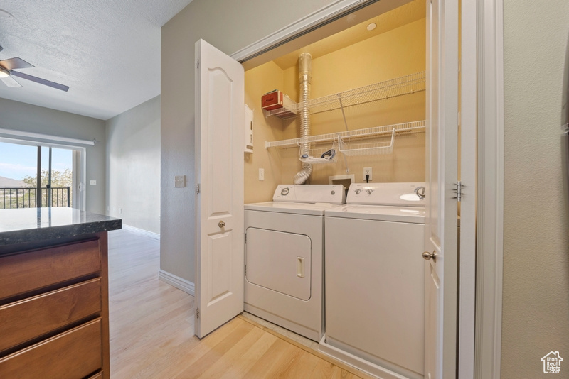 Washroom featuring independent washer and dryer, light wood-type flooring, baseboards, ceiling fan, and a textured ceiling