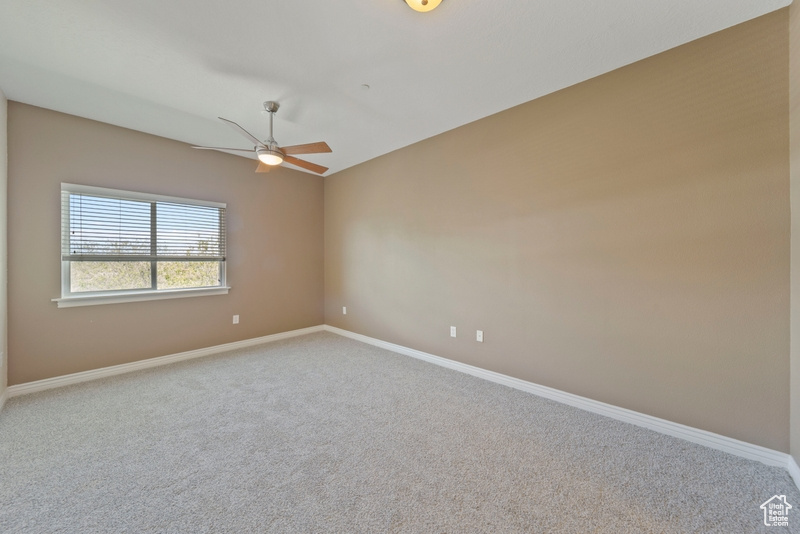 Carpeted empty room featuring a ceiling fan and baseboards