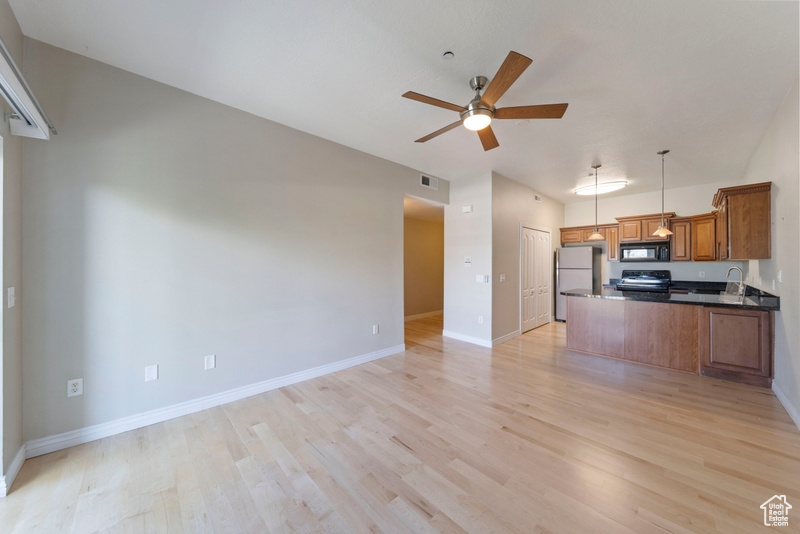 Kitchen featuring appliances with stainless steel finishes, brown cabinets, open floor plan, ceiling fan, and dark countertops