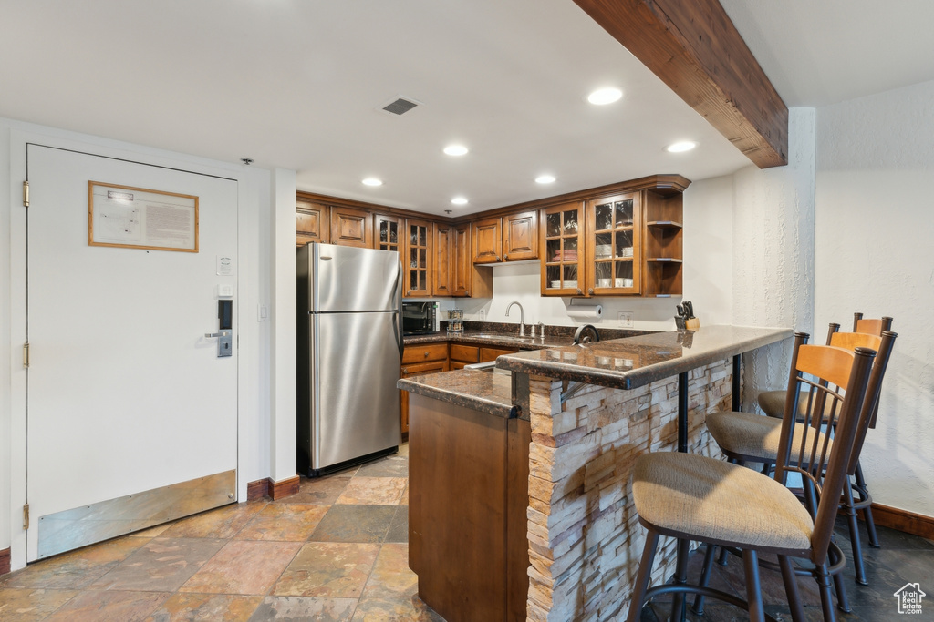 Kitchen with freestanding refrigerator, brown cabinets, a sink, a peninsula, and dark countertops