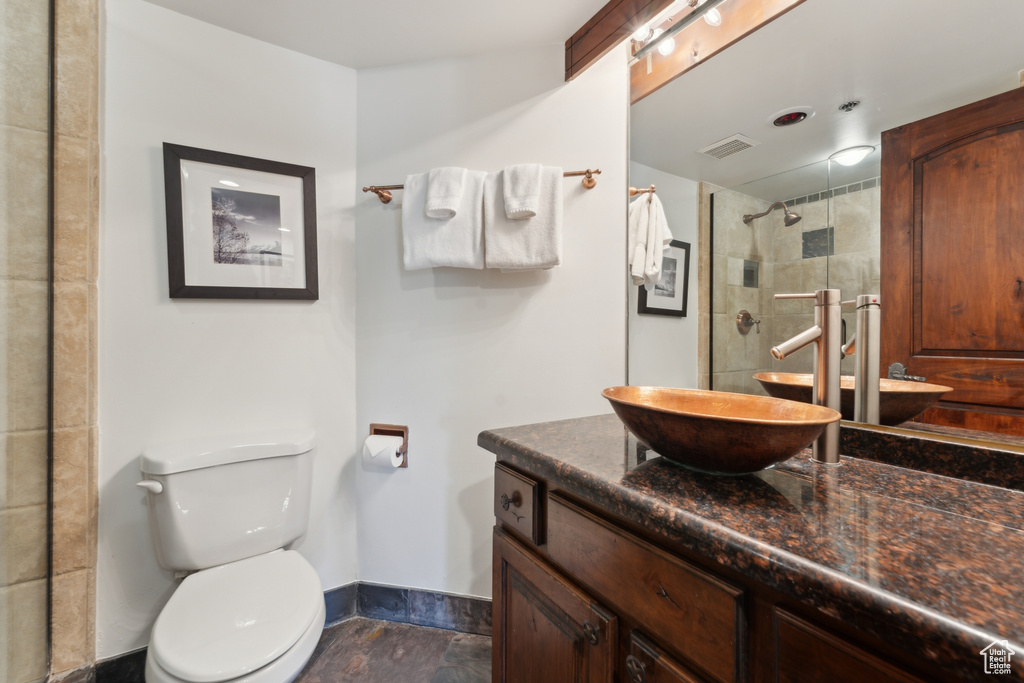 Bathroom featuring a tile shower, vanity, toilet, and baseboards