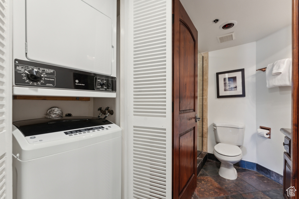 Laundry area featuring stacked washing machine and dryer, baseboards, and dark stone finish floors