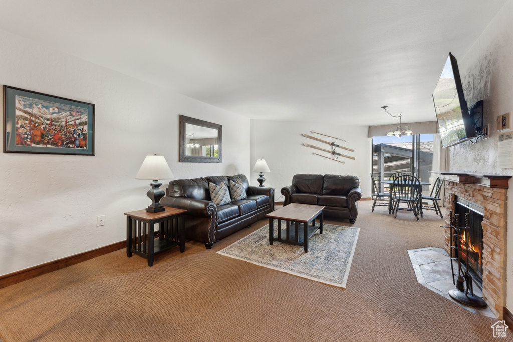 Carpeted living area featuring a fireplace, baseboards, and a chandelier
