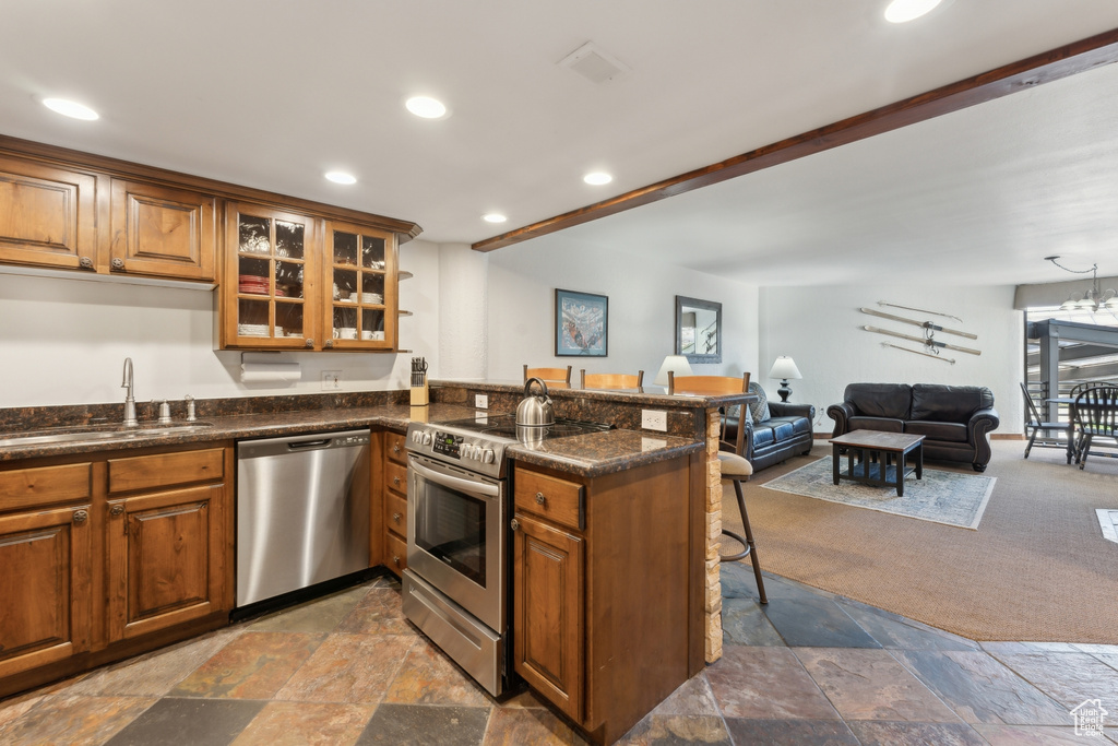 Kitchen with appliances with stainless steel finishes, a sink, brown cabinets, stone tile flooring, and a breakfast bar
