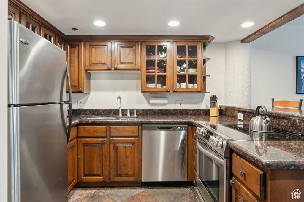 Kitchen featuring appliances with stainless steel finishes, a sink, glass insert cabinets, recessed lighting, and brown cabinetry