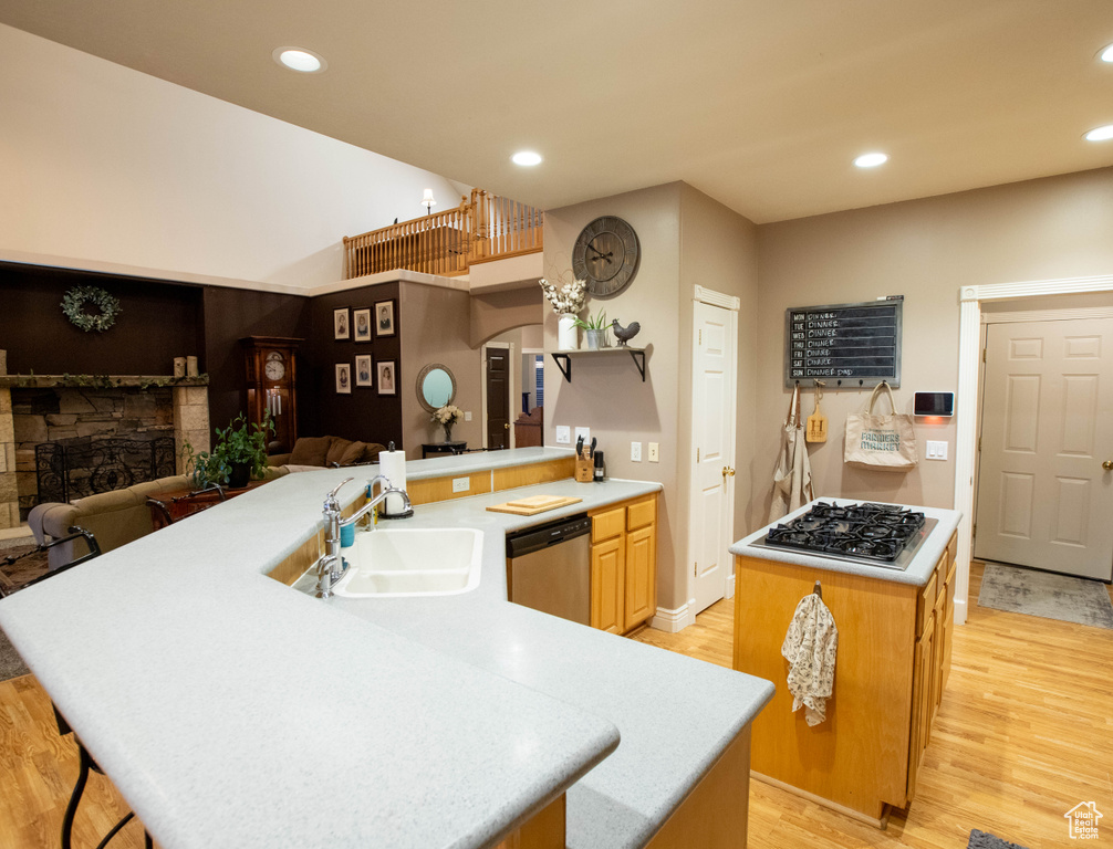 Kitchen featuring appliances with stainless steel finishes, a sink, a kitchen island, a fireplace, and light wood-style flooring