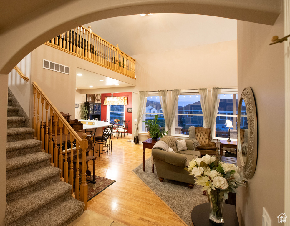 Living area featuring a towering ceiling, stairway, wood finished floors, and arched walkways