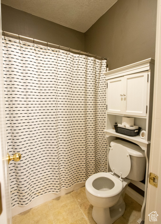 Bathroom with toilet, a textured ceiling, a shower with curtain, and tile patterned floors
