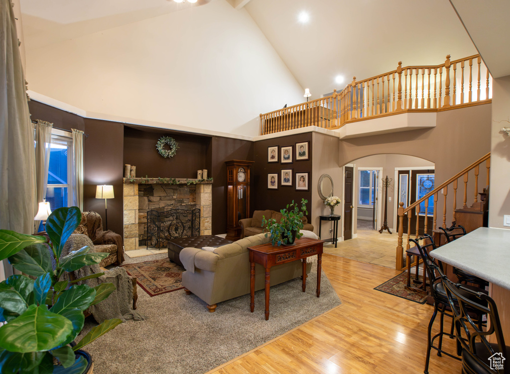 Living room featuring arched walkways, stairway, a stone fireplace, wood finished floors, and high vaulted ceiling
