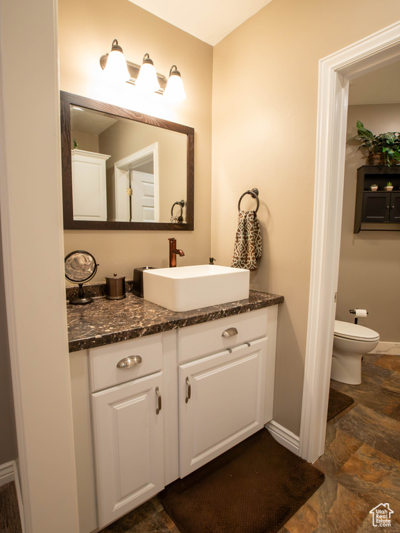 Bathroom with baseboards, stone finish floors, vanity, and toilet