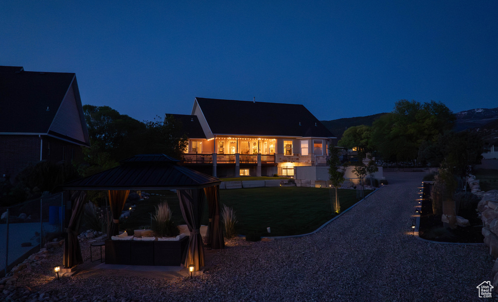 Back of house at night with a gazebo, an outdoor hangout area, and a lawn