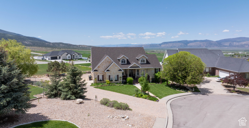 View of front facade with a mountain view, stone siding, a front yard, and a residential view