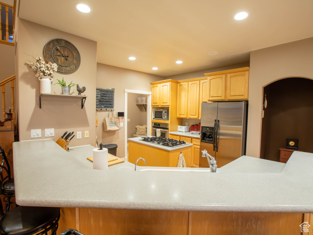 Kitchen featuring stainless steel appliances, light brown cabinets, a peninsula, recessed lighting, and a kitchen bar