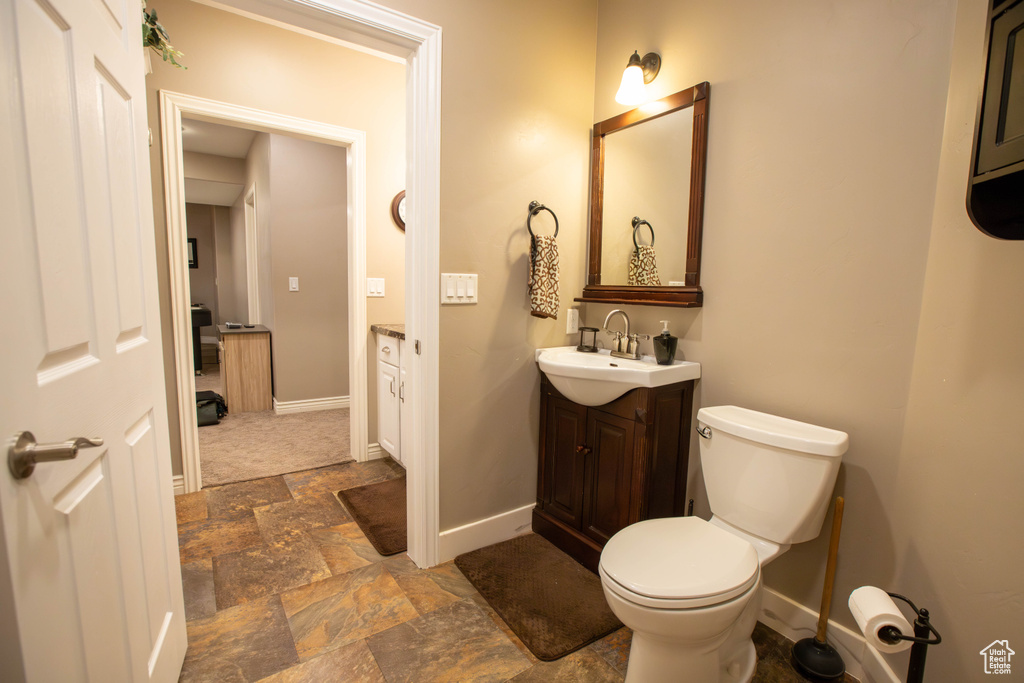 Bathroom featuring baseboards, stone finish flooring, vanity, and toilet