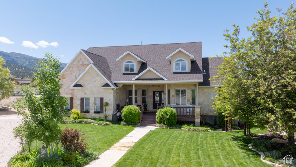Traditional-style home with stone siding, a porch, roof with shingles, a front lawn, and a mountain view