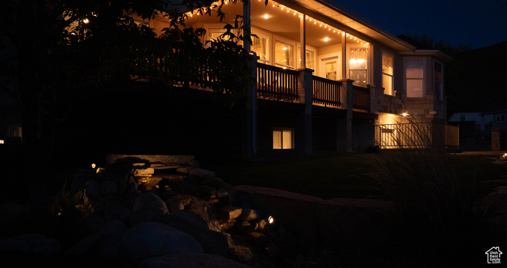 Back of house at twilight featuring stone siding