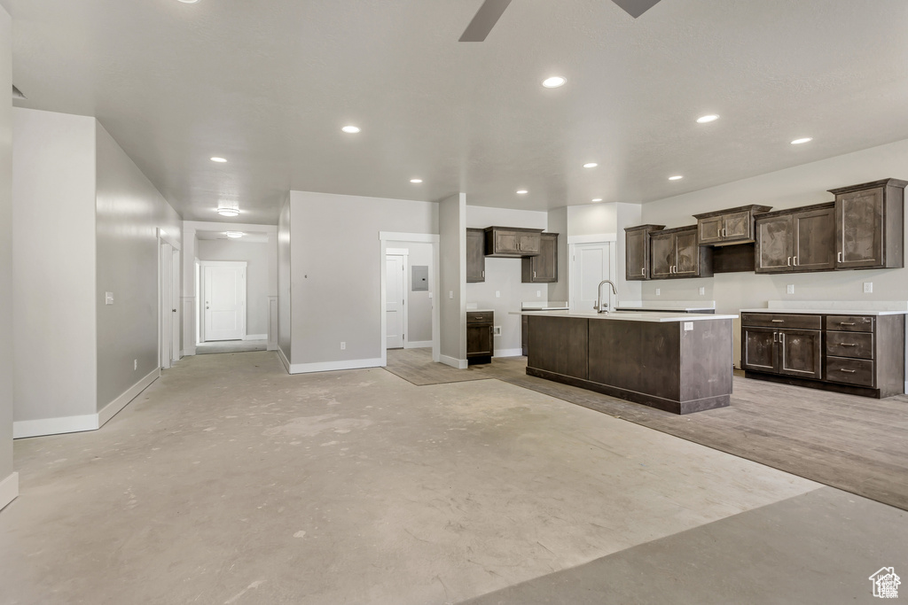 Kitchen featuring dark brown cabinetry, a sink, recessed lighting, baseboards, and a center island with sink