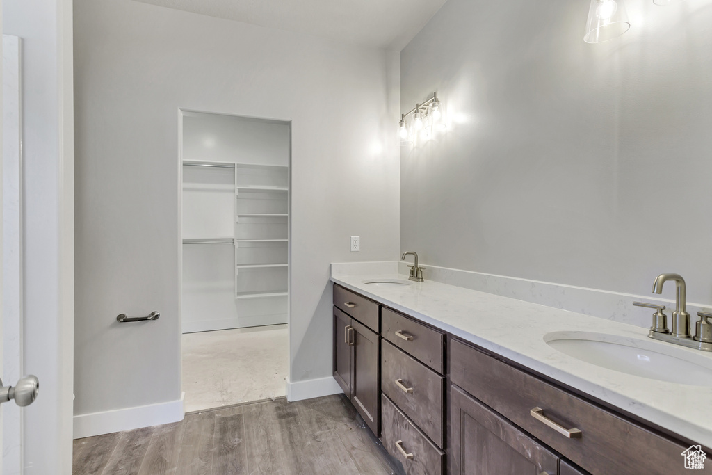 Bathroom with wood finished floors, a walk in closet, double vanity, and baseboards