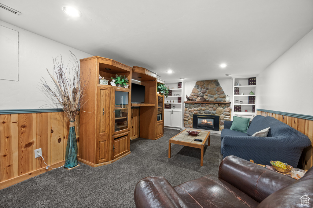 Living room featuring dark colored carpet, wainscoting, wood walls, a stone fireplace, and built in features