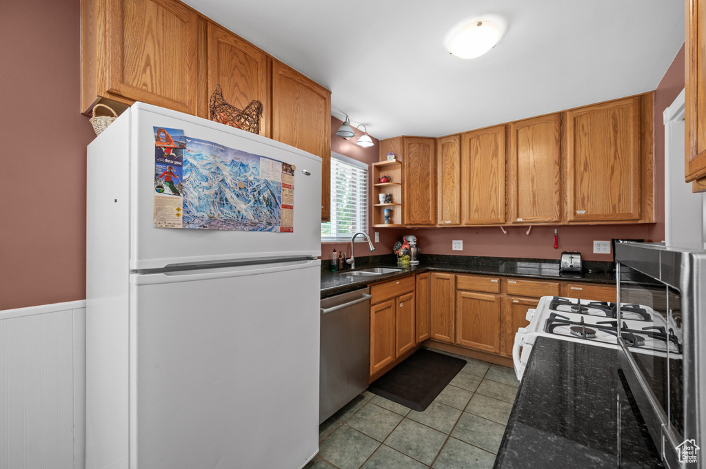 Kitchen featuring freestanding refrigerator, stainless steel dishwasher, a sink, light tile patterned flooring, and open shelves