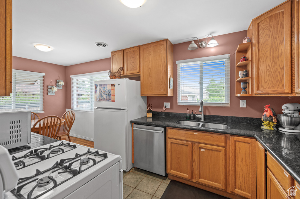 Kitchen with white appliances, a sink, dark stone countertops, light tile patterned flooring, and brown cabinetry