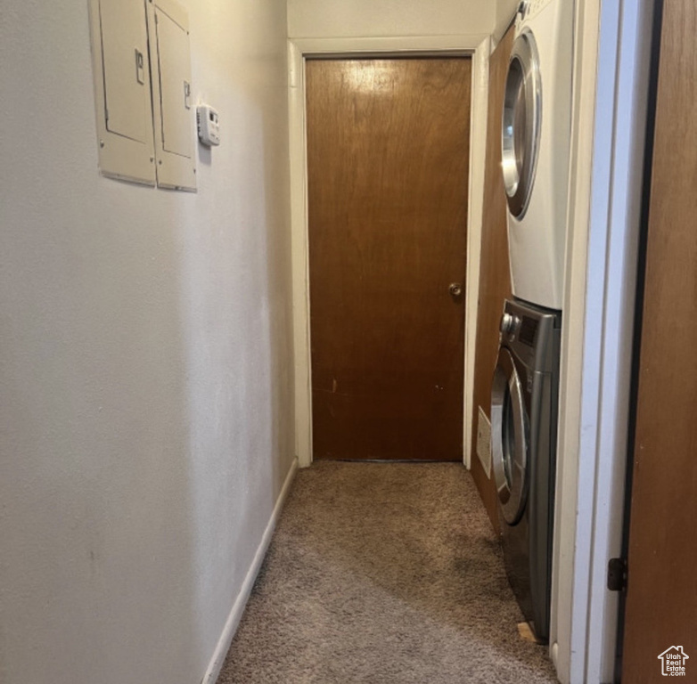 Washroom with stacked washing machine and dryer, carpet, electric panel, and baseboards
