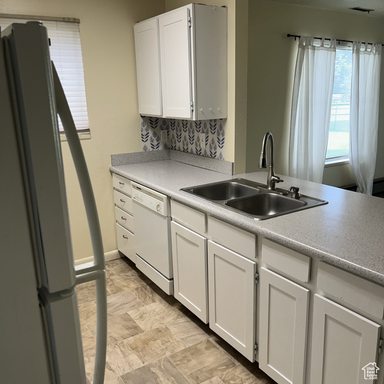 Kitchen with white appliances, white cabinets, light countertops, and backsplash