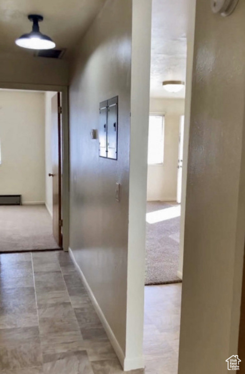 Corridor with electric panel, carpet floors, baseboards, and a baseboard heating unit