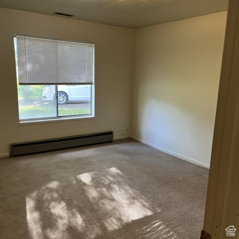 Carpeted spare room featuring a baseboard heating unit and baseboards