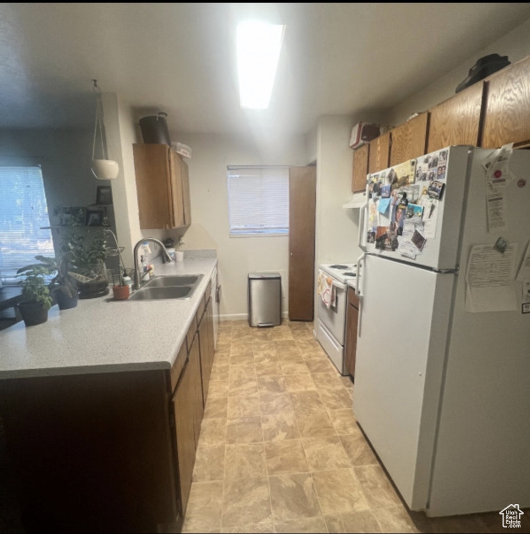 Kitchen featuring white appliances, a sink, light countertops, brown cabinetry, and under cabinet range hood