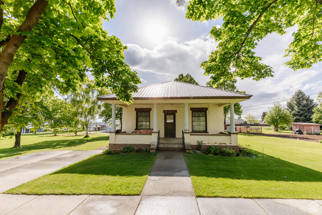 Bungalow with brick siding, a porch, a front lawn, and metal roof