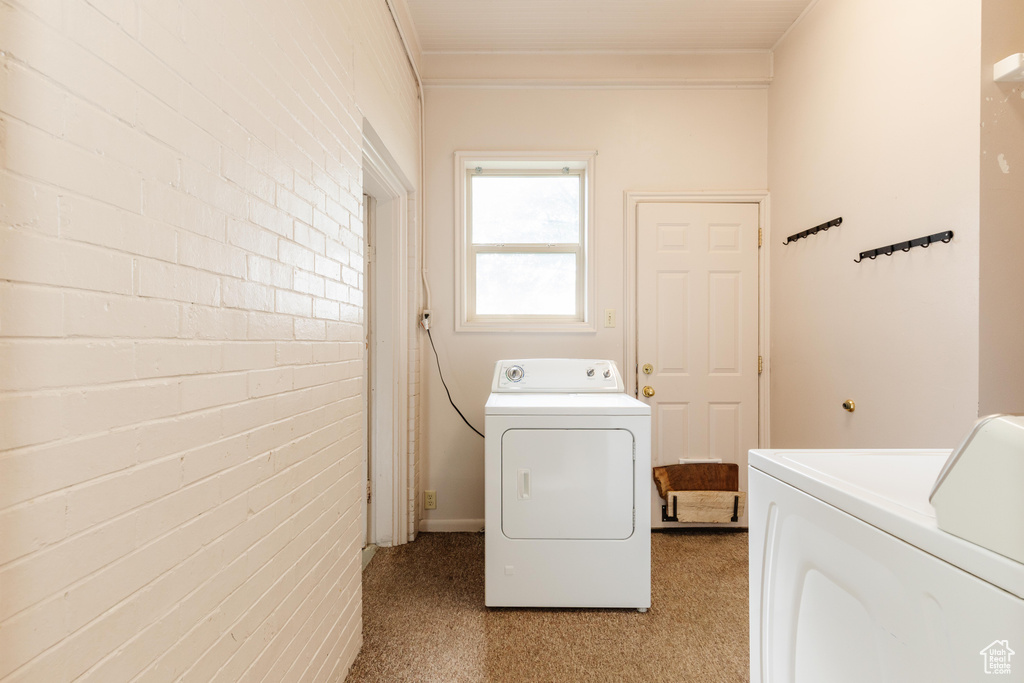 Washroom featuring washing machine and dryer, brick wall, and ornamental molding