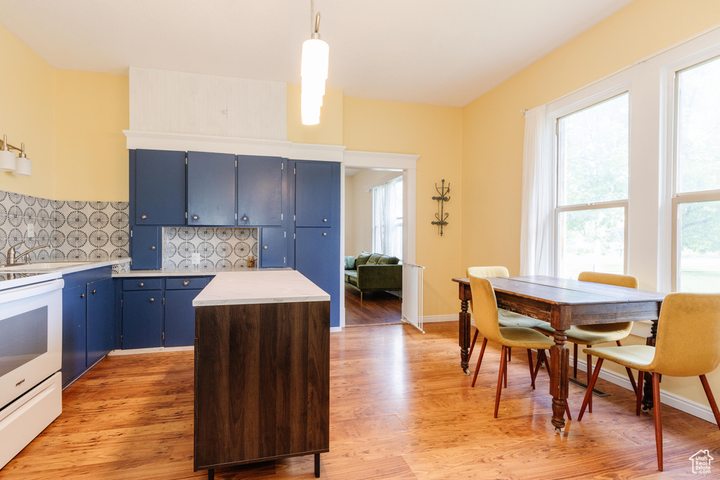 Kitchen with blue cabinetry, white range with electric stovetop, light countertops, decorative backsplash, and light wood-style flooring