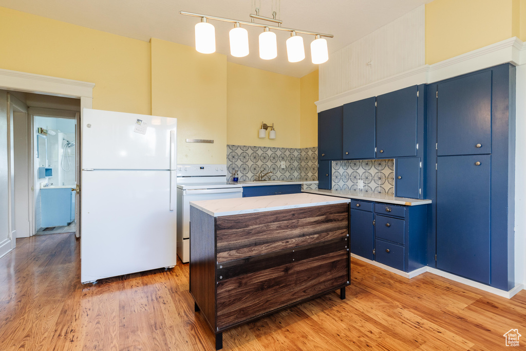 Kitchen with white appliances, blue cabinetry, light countertops, decorative backsplash, and light wood-style floors
