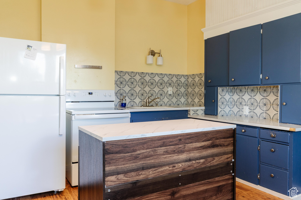 Kitchen featuring white appliances, blue cabinets, a sink, tasteful backsplash, and light wood-type flooring