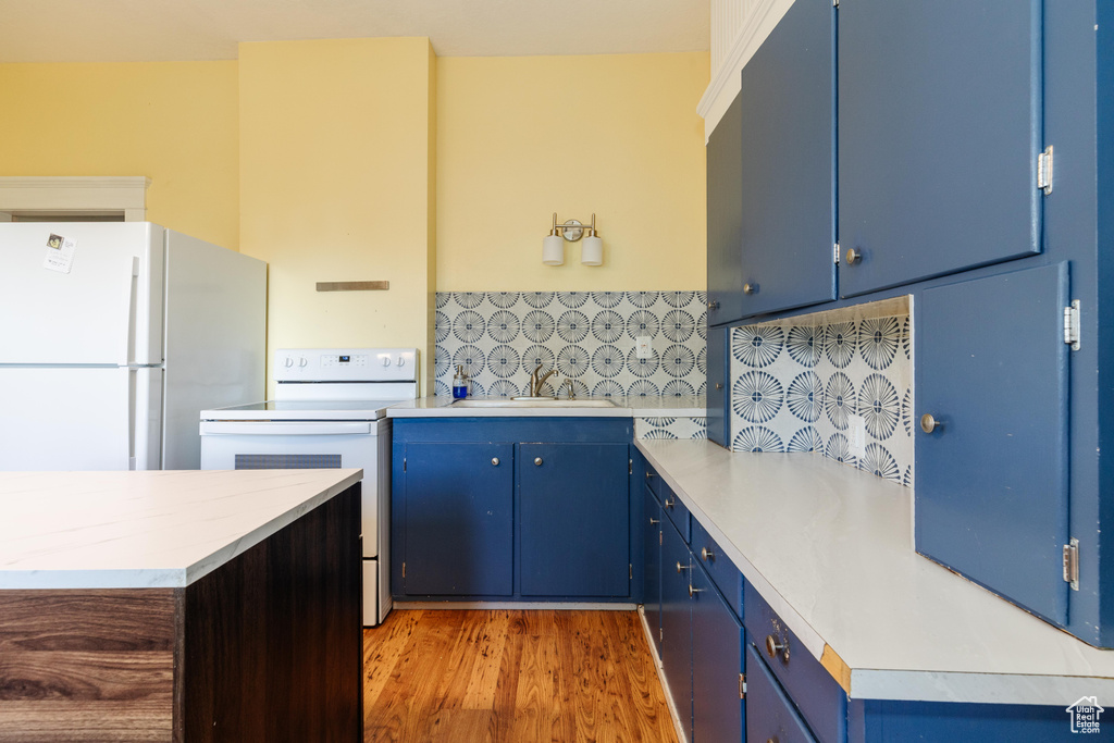 Kitchen featuring white appliances, a sink, blue cabinets, and light countertops