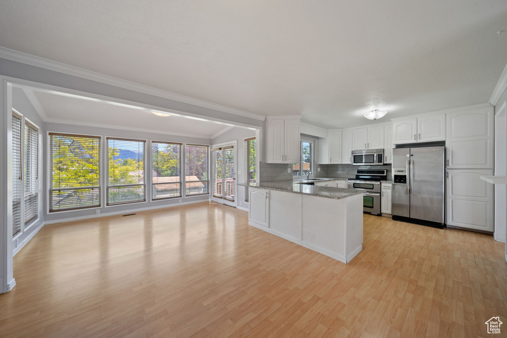 Kitchen featuring appliances with stainless steel finishes, a sink, light wood-style floors, white cabinetry, and a peninsula