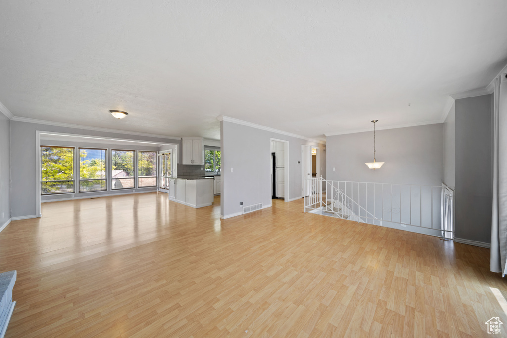 Unfurnished living room with ornamental molding, light wood-style floors, and baseboards