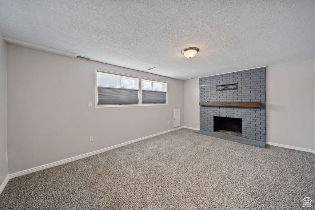 Unfurnished living room featuring a fireplace, a textured ceiling, carpet floors, and baseboards