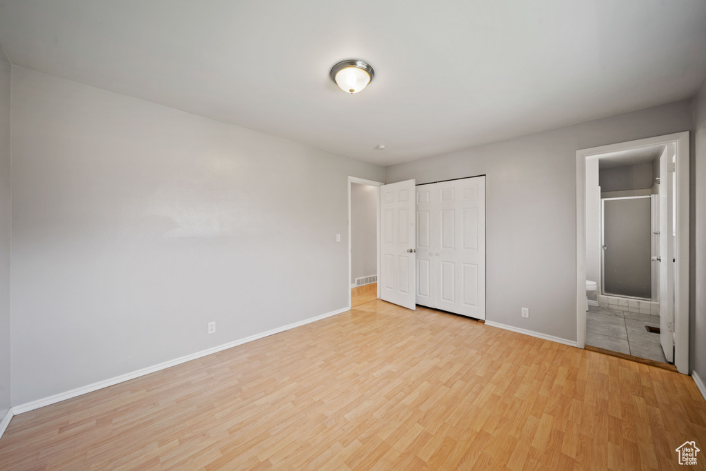 Unfurnished bedroom featuring light wood-style floors, baseboards, a closet, and connected bathroom