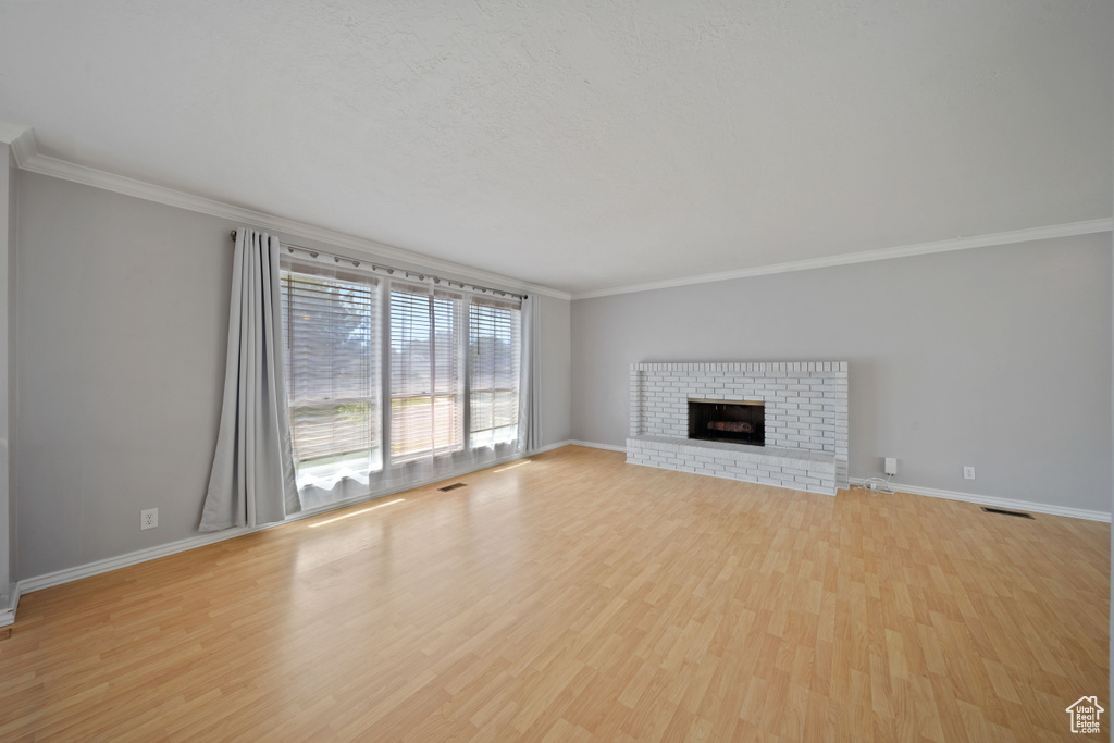 Unfurnished living room featuring crown molding, light wood-style floors, baseboards, and a brick fireplace