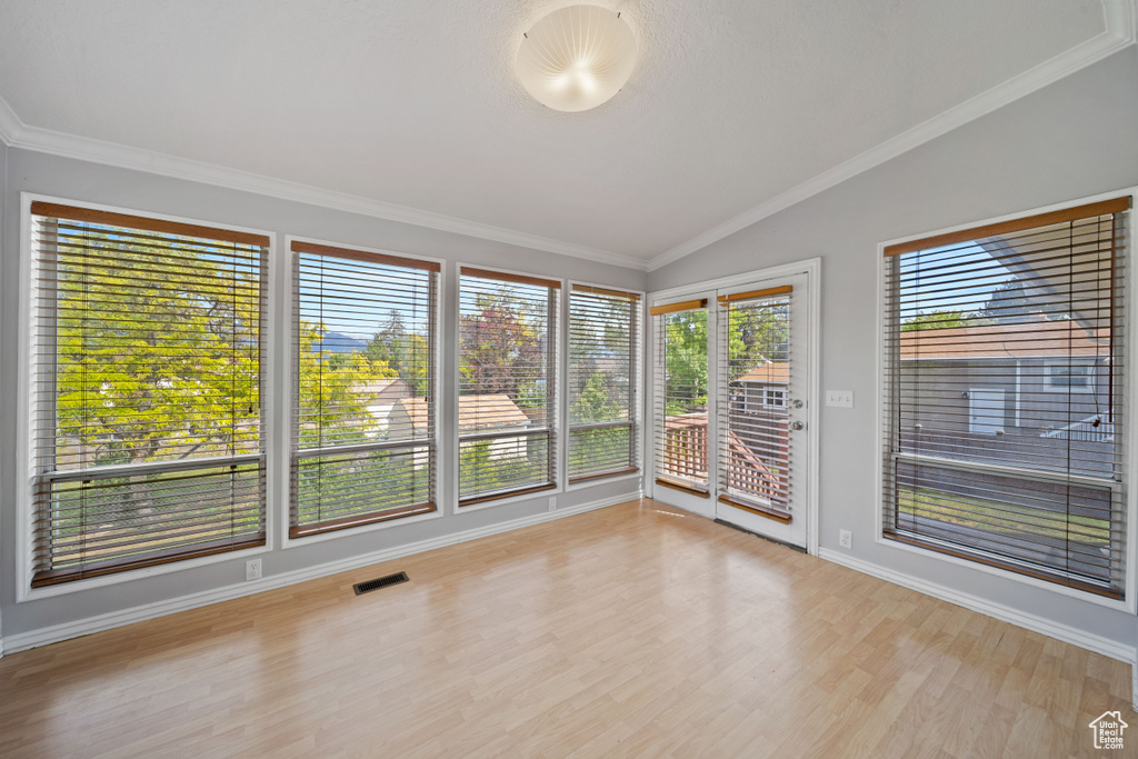 Unfurnished sunroom with lofted ceiling, wood finished floors, ornamental molding, and baseboards