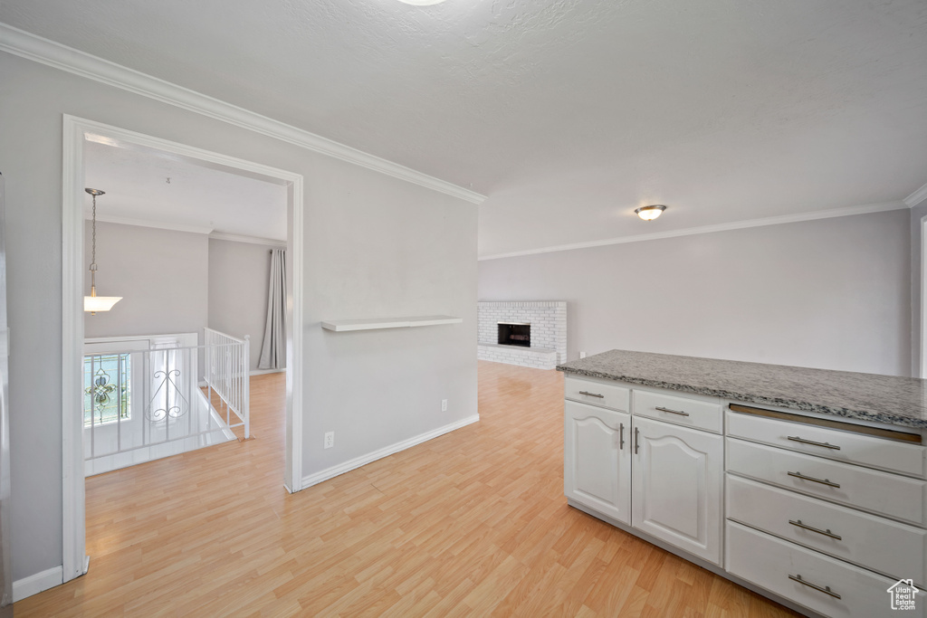 Kitchen featuring ornamental molding, light wood-style flooring, white cabinets, baseboards, and a brick fireplace