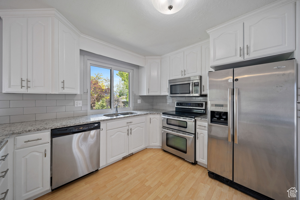 Kitchen with stainless steel appliances, a sink, light wood-style flooring, tasteful backsplash, and white cabinetry