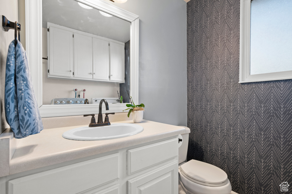 Bathroom featuring wallpapered walls, an accent wall, toilet, and vanity