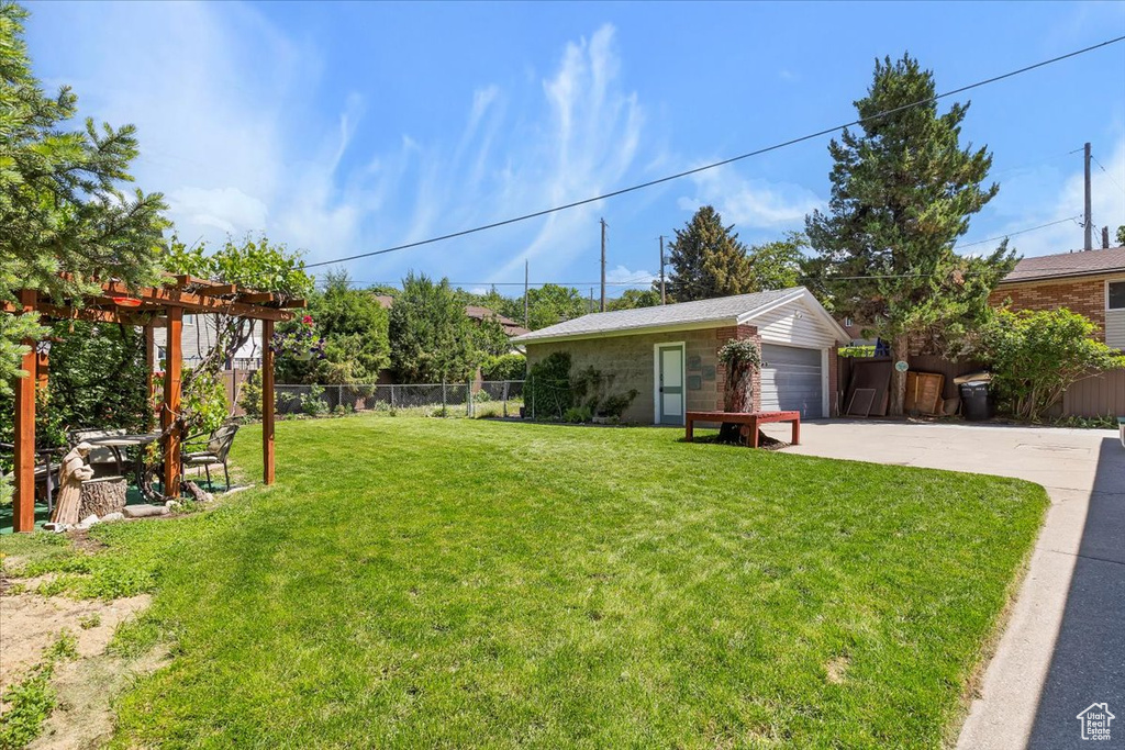 View of yard with a pergola, a garage, and concrete driveway