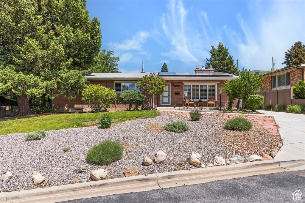 Ranch-style home with brick siding, roof mounted solar panels, covered porch, driveway, and a front yard