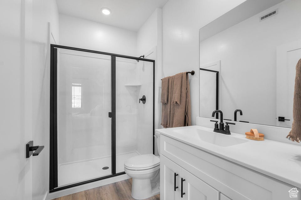 Bathroom featuring a stall shower, wood finished floors, vanity, and toilet