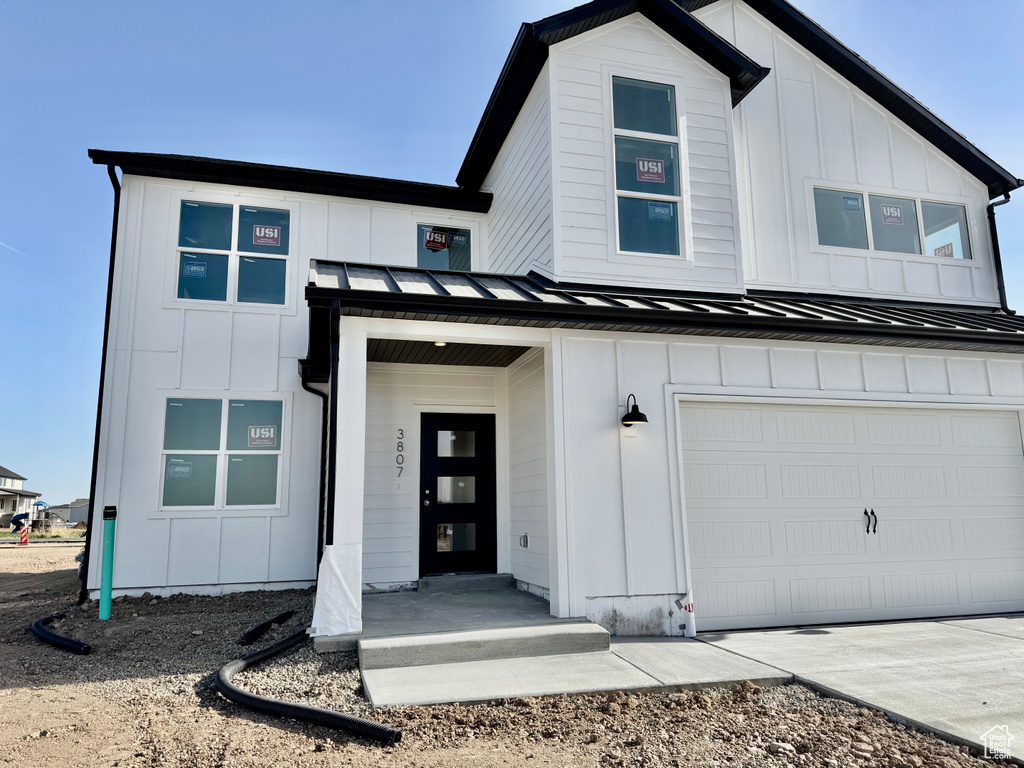 View of front facade with a standing seam roof, board and batten siding, an attached garage, metal roof, and concrete driveway