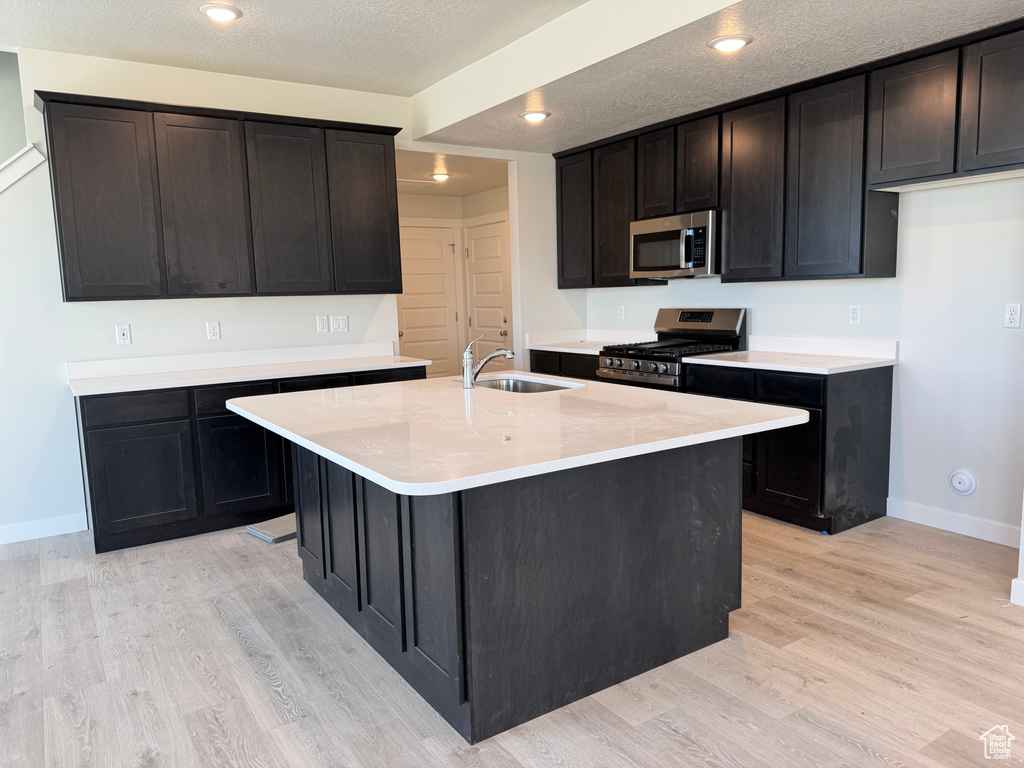 Kitchen featuring appliances with stainless steel finishes, a sink, baseboards, light wood finished floors, and light countertops
